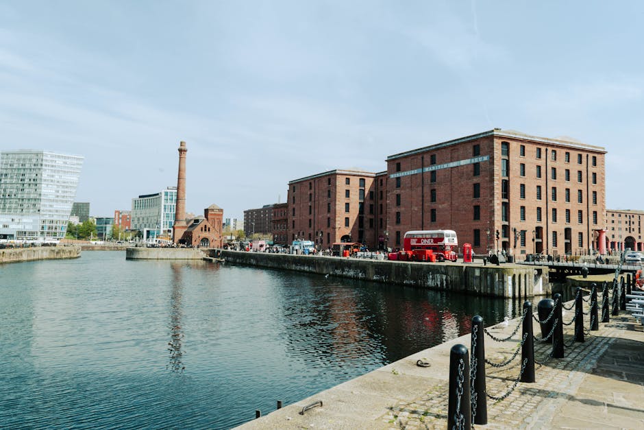 A nighttime view of Liverpool's Albert Dock area showing illuminated historic brick buildings on the left, with modern high-rise office buildings and skyscrapers further along the waterfront on the ri
